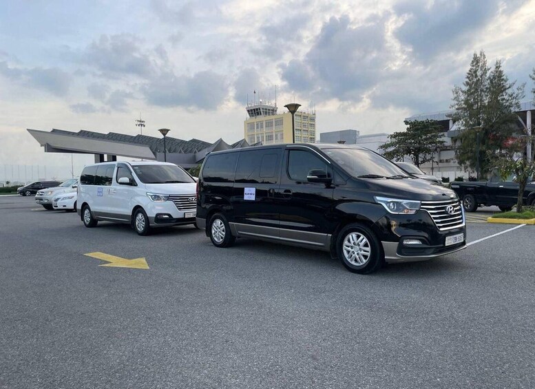 A parking lot with two minivans, one black and one white, parked near a building with a distinctive roof. 3