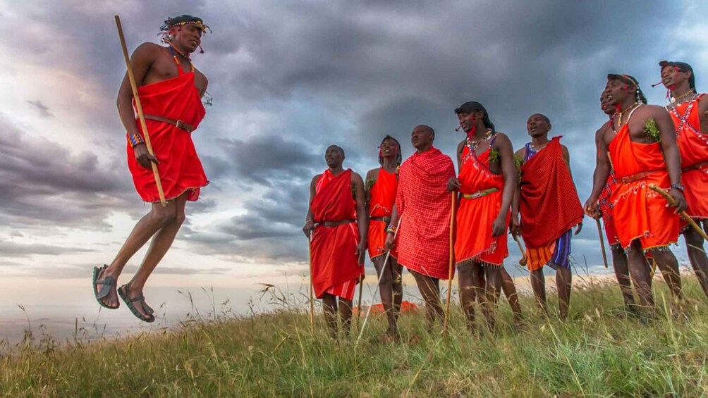 Maasai warriors in red attire standing in a grassy field with a cloudy sky. 4