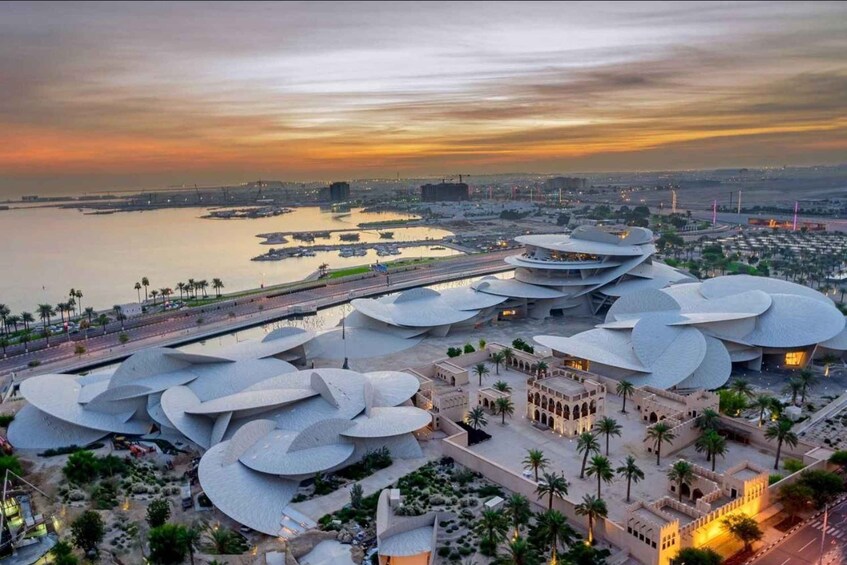 A modern architectural complex with unique curved structures, a waterfront, and a sunset sky. 1