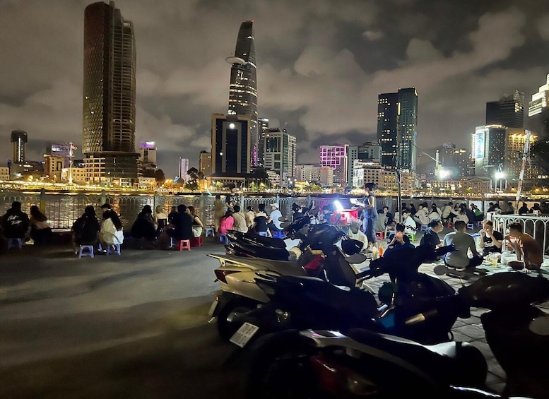 A nighttime cityscape with people gathered on a bridge, overlooking a river and tall buildings. 5