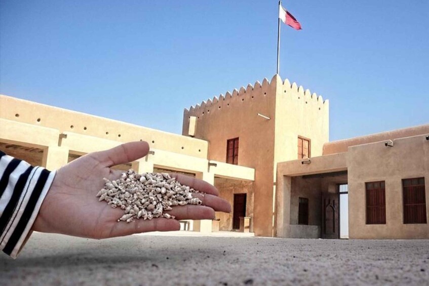 A hand holding grains in front of a building with a flag. 3