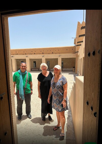 Three people standing in an outdoor courtyard with beige walls and a clear sky. 4
