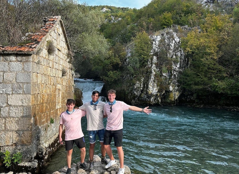 Three people standing by a stone wall with a river and waterfall in the background. 3