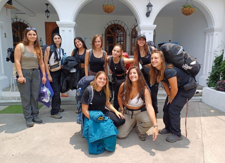 A group of people posing in front of a white building with arched windows and hanging plants. 1