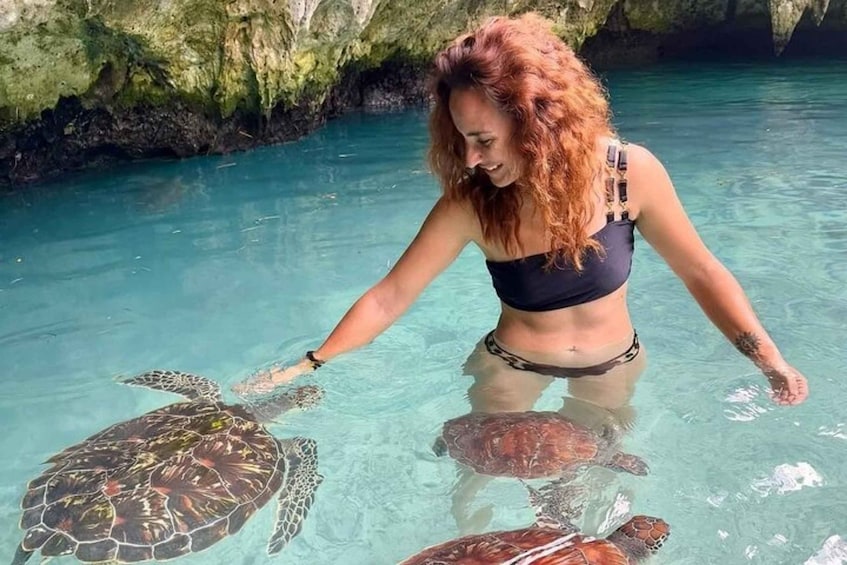 A person in a black swimsuit interacting with sea turtles in clear blue water. 1