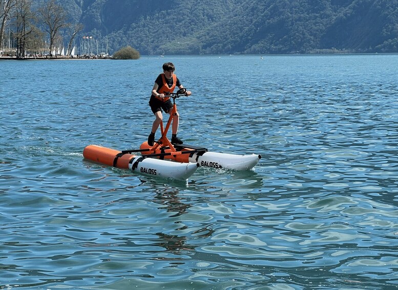 A person riding a small white and orange paddleboard on calm water. 3