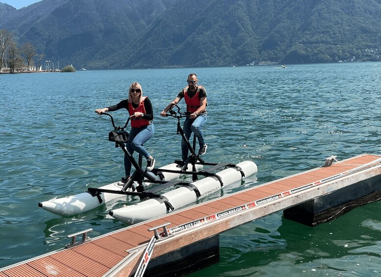 Two people riding water bikes on a dock by a lake with mountains in the background. 4