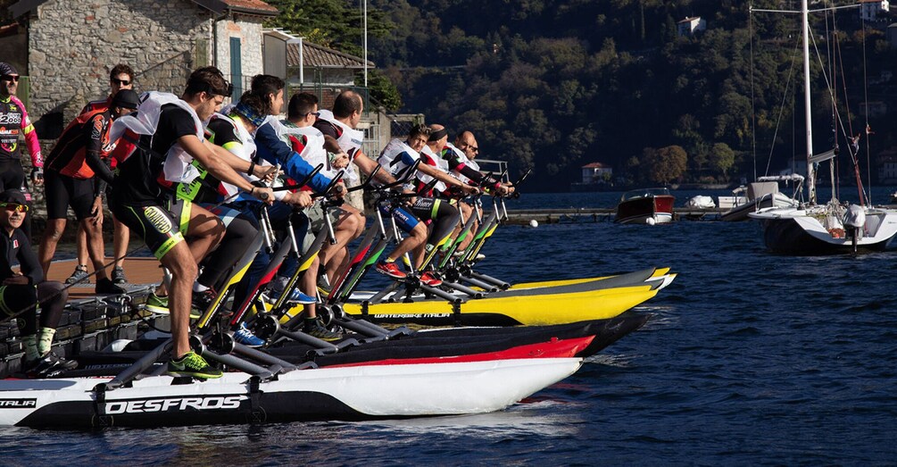 A group of cyclists on water bikes, lined up on a dock by the water. 5