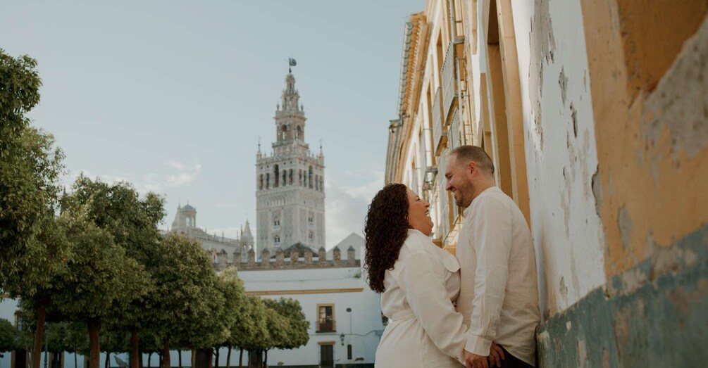 A couple standing by a building with a historic tower in the background. 1