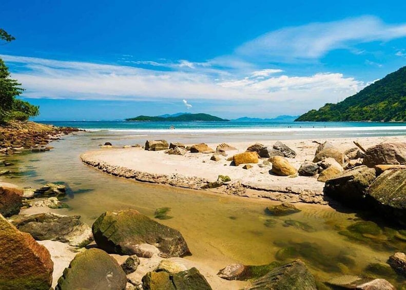 A rocky beach with clear water, a sandy area, and distant mountains. 1