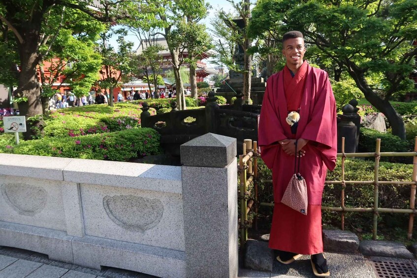 A person in traditional attire standing by a stone structure with a garden in the background. 4