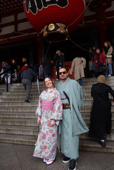 A person in a kimono and another in a light blue robe standing on stone steps with a red lantern overhead. 5