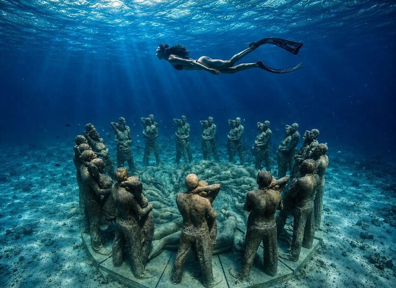 A diver swimming above a submerged stone circle with ancient statues. 1