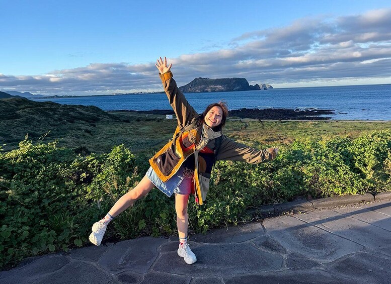 A person posing with arms outstretched, a rocky coastline, and a clear sky in the background. 1