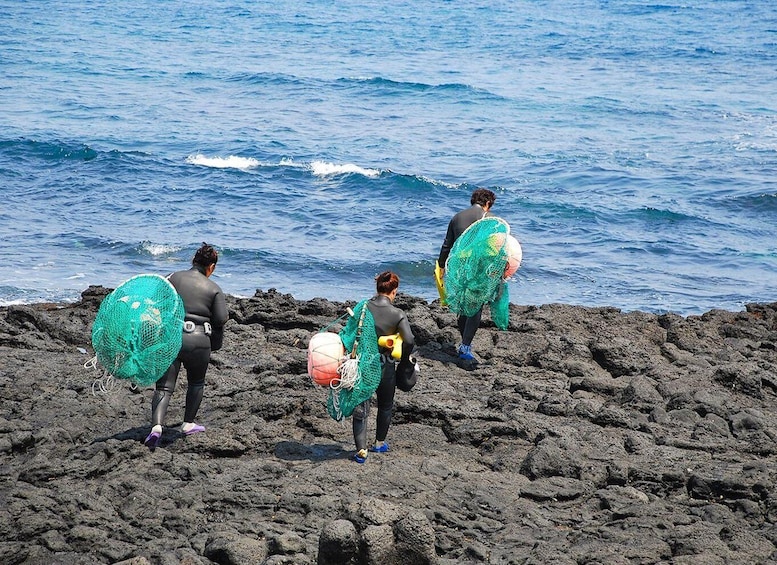 Three people on a rocky shoreline with surfboards, standing by the ocean. 1