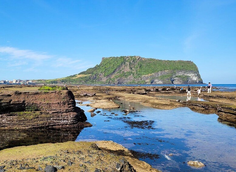 A coastal landscape with rocky formations, a cliff, and a beach with people. 5