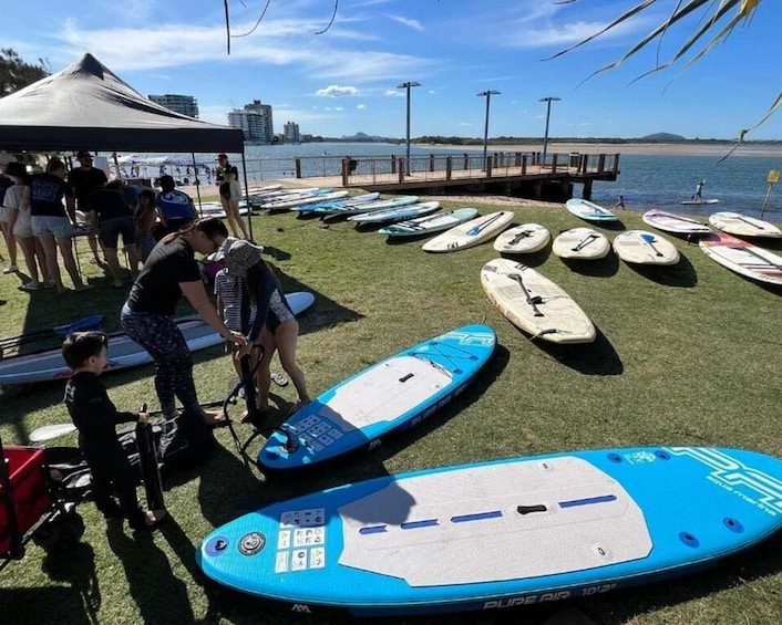 A group of people at a beach with surfboards lined up on the grass. 1