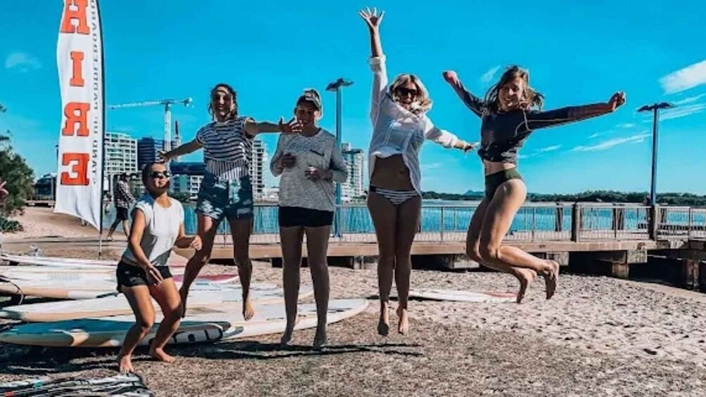 A group of people jumping on a beach with surfboards and a lifeguard tower in the background. 2