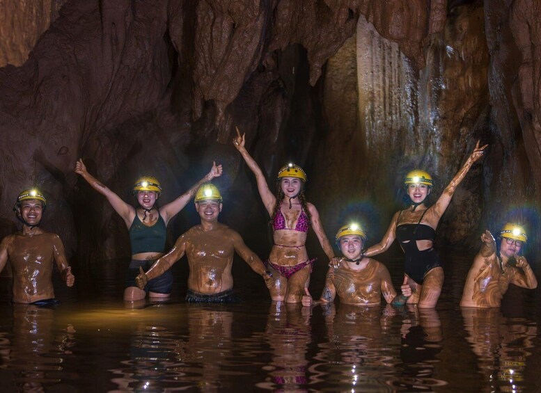 A group of people in a cave with water, wearing helmets and covered in mud. 3