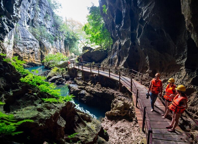 A group of people in orange life vests standing on a wooden bridge over a river in a rocky canyon. 4