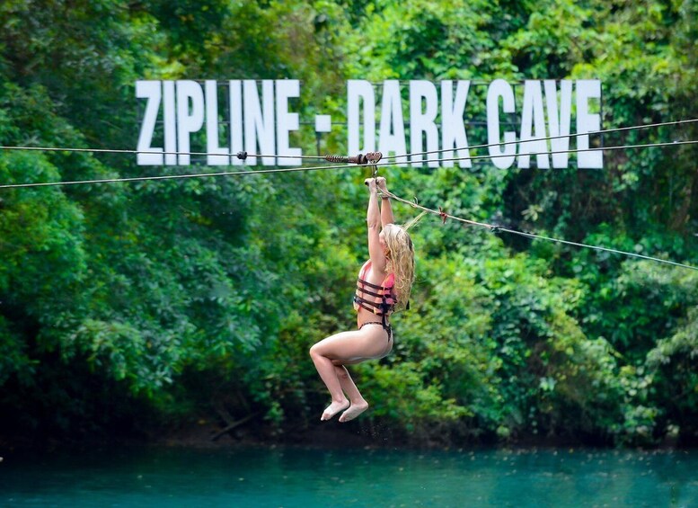 A person ziplining over a river with a sign reading "ZIPLINE - DARK CAVE" in the background. 2