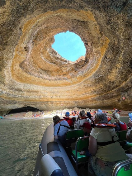 A group of people in a boat observing a large spiral rock formation. 1