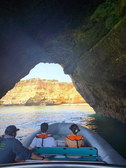 A boat with three people wearing life jackets, navigating through a natural rock arch formation. 4