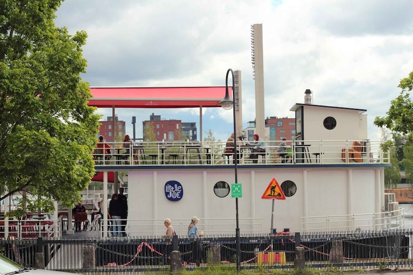 A riverside restaurant with outdoor seating, a red awning, and a warning sign. 2