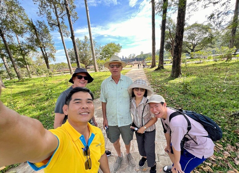 A group of people taking a selfie in a park with trees and a pathway. 2