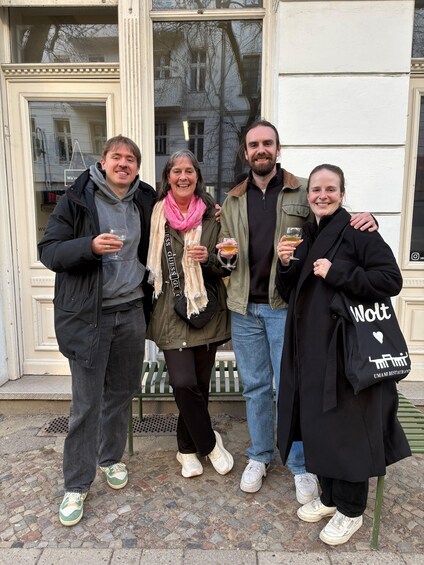Four people standing in front of a building with a white facade and a window reflecting trees. 1