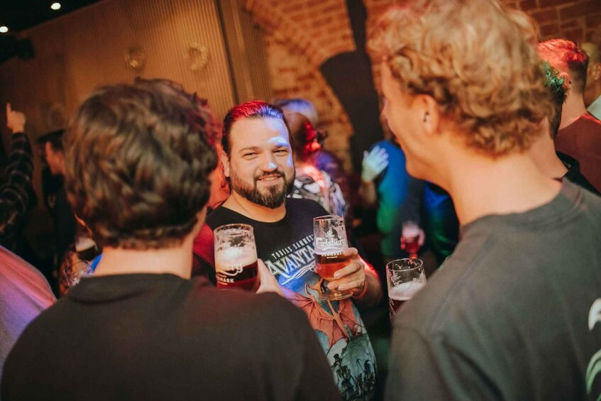 Un groupe de personnes se trouve dans un endroit intérieur à la lumière tamisée, peut-être un bar ou un pub, avec des murs en briques et une foule de personnes. 2