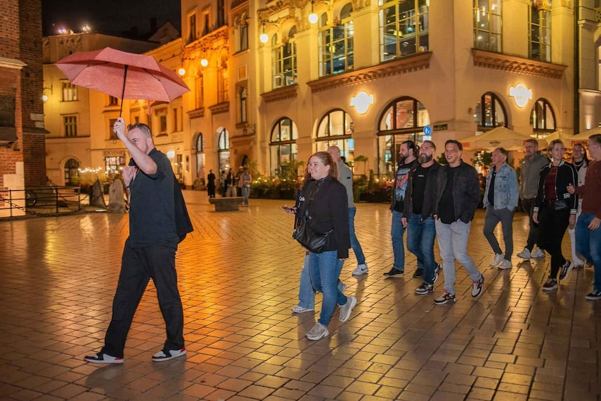 Un groupe de personnes marchant sur un trottoir pavé la nuit, avec un bâtiment doté de fenêtres en arc de cercle et d’un éclairage chaleureux en arrière-plan. 5