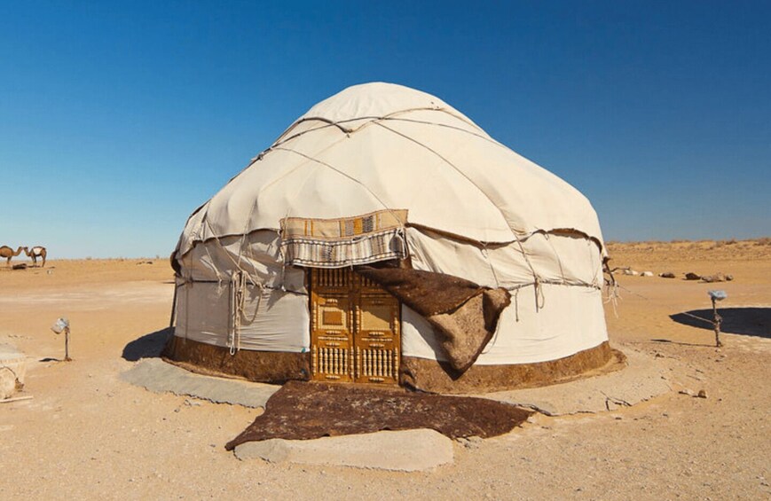 A traditional yurt with a wooden door, set in a desert landscape. 2