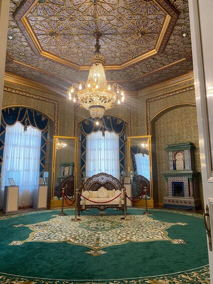 An opulent room with a large ornate bed, a chandelier, and intricate ceiling and wall designs. 3