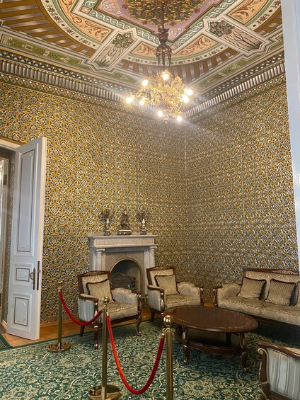 An opulent room with ornate wallpaper, a grand chandelier, and a fireplace. 5