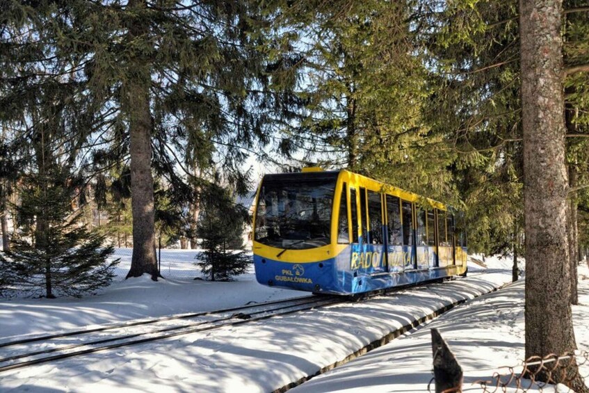 A yellow and blue tram in a snowy forest. 3