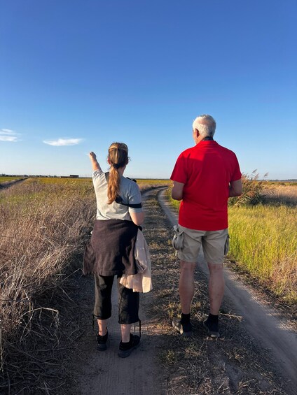 Two people walking on a dirt path in a field with tall grass and a clear blue sky. 2