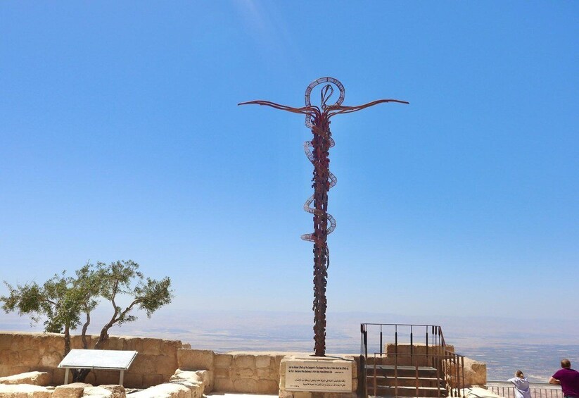 A tall metal sculpture with a circular top and long, curved extensions, set against a clear blue sky. 5