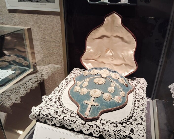 A decorative item with a cross and floral design, displayed on a lace-covered stand. 2