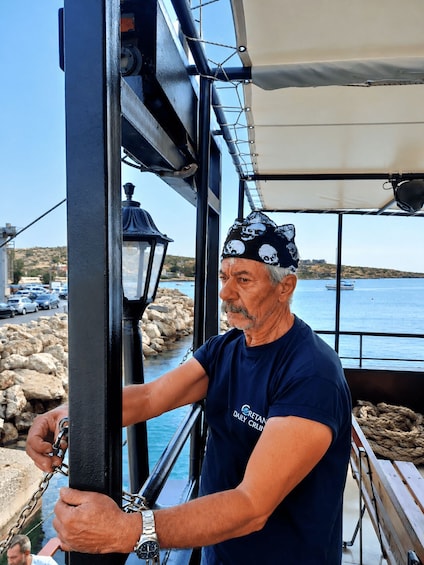 A man on a boat, wearing a bandana and a t-shirt, holding onto a metal structure. 2