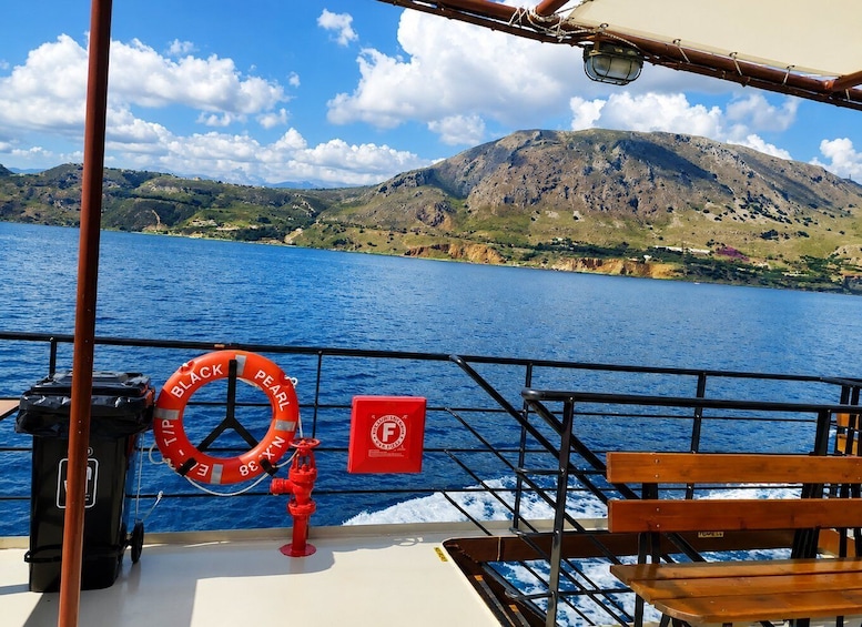 A boat deck with a life buoy, a red box, and a view of a mountainous coastline. 4