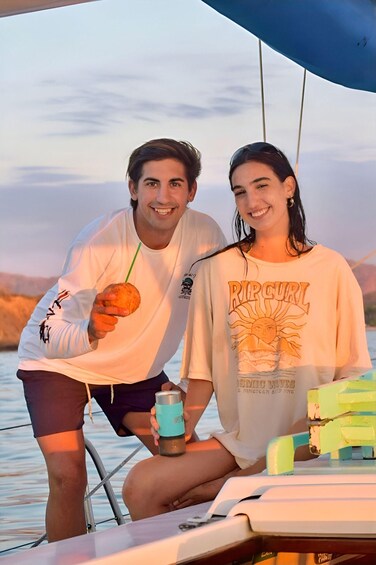 Two people on a boat, one holding a drink and the other holding a snack. 2