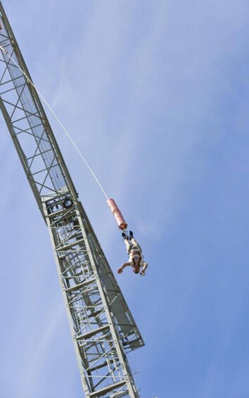 A bungee jumper suspended from a tall metal structure against a clear sky. 2