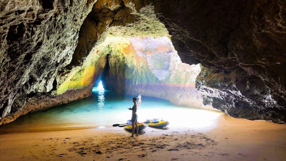 A cave with a rainbow-colored interior and a person standing on the beach. 1