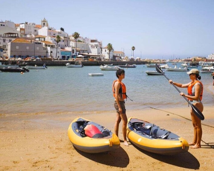 Two people on a beach with kayaks, a marina in the background, and buildings along the shore. 4