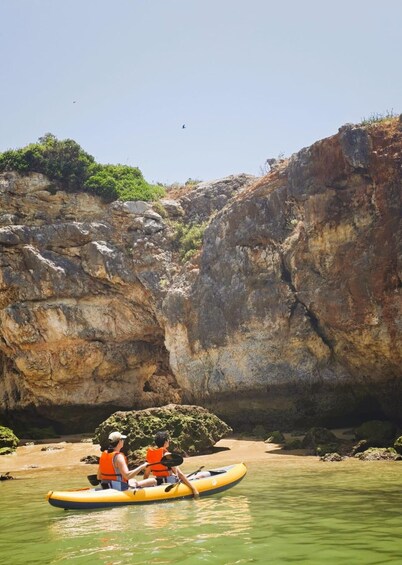 Two people kayaking on a calm river with rocky cliffs in the background. 5