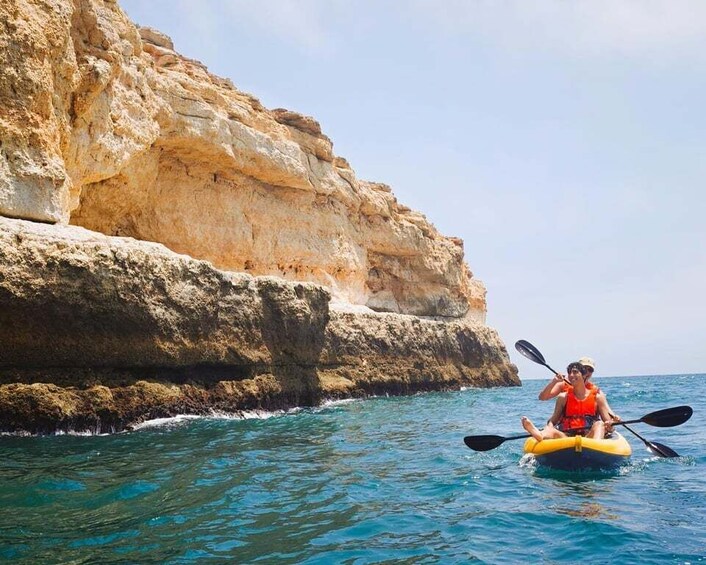 A person kayaking on clear blue waters with a rocky cliff in the background. 2