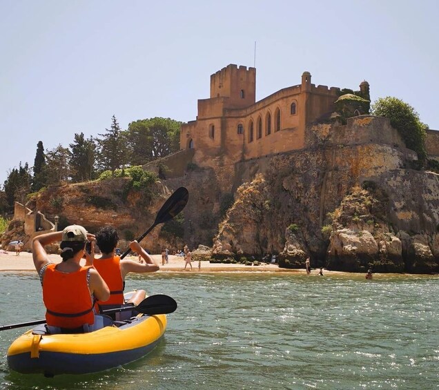 A couple kayaking on a calm body of water with a historic castle on a rocky cliff in the background. 3