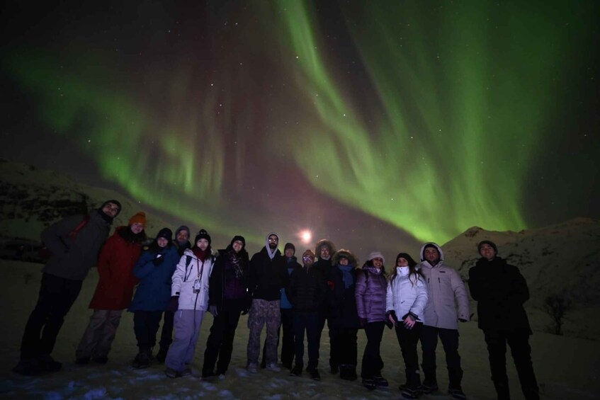 A group of people standing in a snowy landscape under a night sky with green aurora borealis. 1