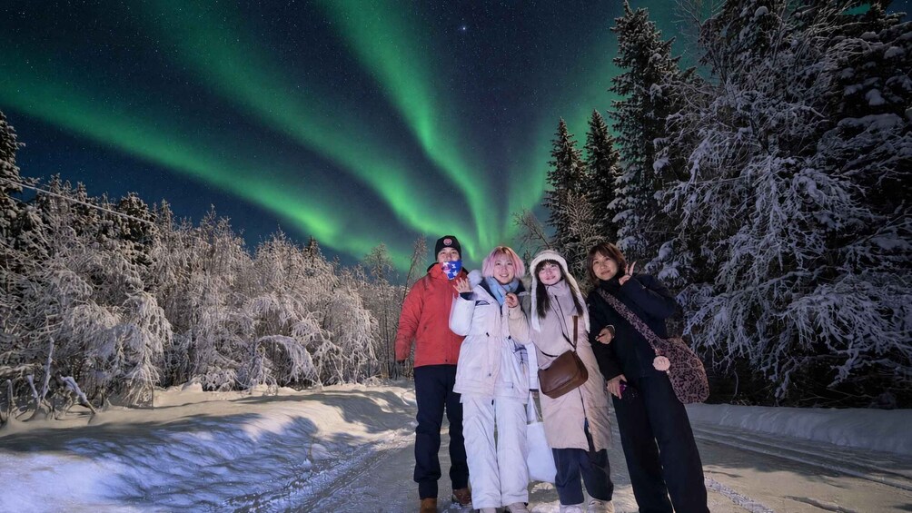 A group of people posing in front of the Northern Lights with snow-covered trees in the background. 4